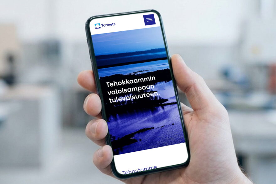 Tormetsin WordPress-verkkosivut puhelimen n&auml;yt&ouml;ll&auml; k&auml;dess&auml;, taustalla sumea teollisuustila