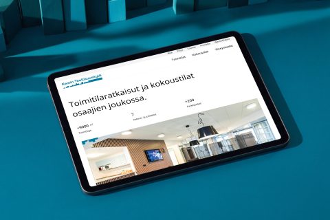 Kemin Teollisuuskylän verkkosivut tabletin näytöllä petroolinsinisellä pöydällä, esillä toimitilat ja kokoustilat