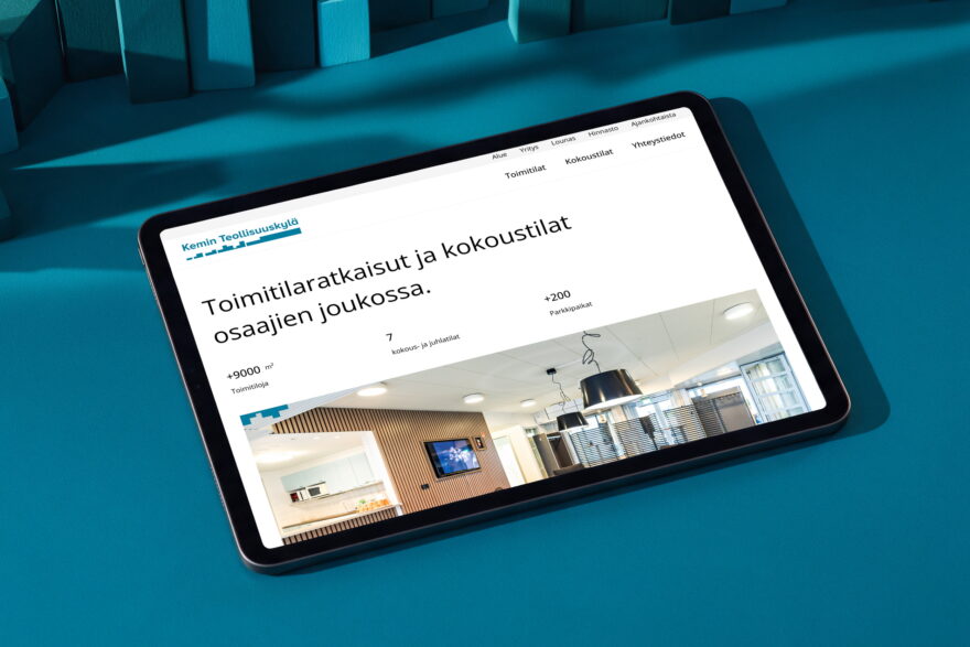 Kemin Teollisuuskyl&auml;n verkkosivut tabletin n&auml;yt&ouml;ll&auml; petroolinsinisell&auml; p&ouml;yd&auml;ll&auml;, esill&auml; toimitilat ja kokoustilat