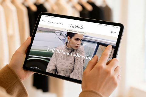 Tornion La Perlen WooCommerce-verkkokauppa tabletin näytöllä käsissä vaatetankojen edessä
