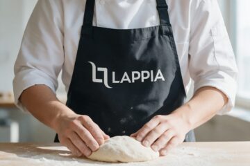 Lappian valkoinen logo mustassa essussa leipurin vaivatessa taikinaa