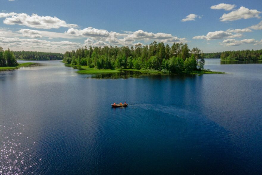 Mets&auml;inen saari ja vene sinisell&auml; j&auml;rvell&auml; kes&auml;p&auml;iv&auml;n&auml;