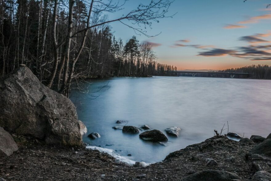 Kallioranta ja kivi&auml; tyynell&auml; j&auml;rvell&auml; illalla, taustalla silta