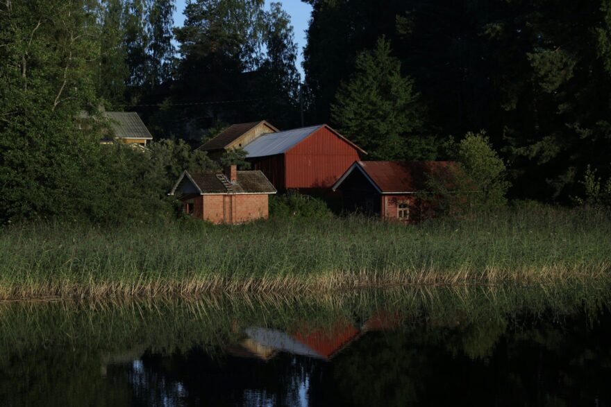 Punaisia ulkorakennuksia j&auml;rven rannalla kes&auml;illan valossa
