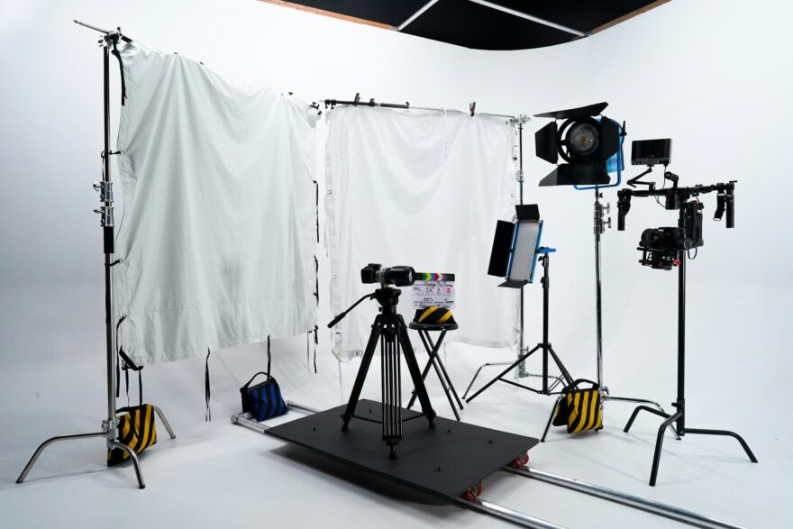Kuvausstudio, jossa videokamera jalustalla, valaisimet ja heijastinkankaat