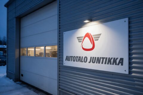 Autotalo Juntikan logo korjaamon seinäkyltissä iltahämärässä
